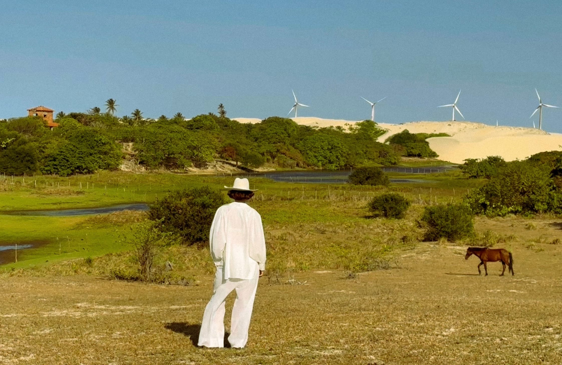 Pessoa observando a paisagem de Lençóis com lagoa, vegetação e dunas ao fundo.
